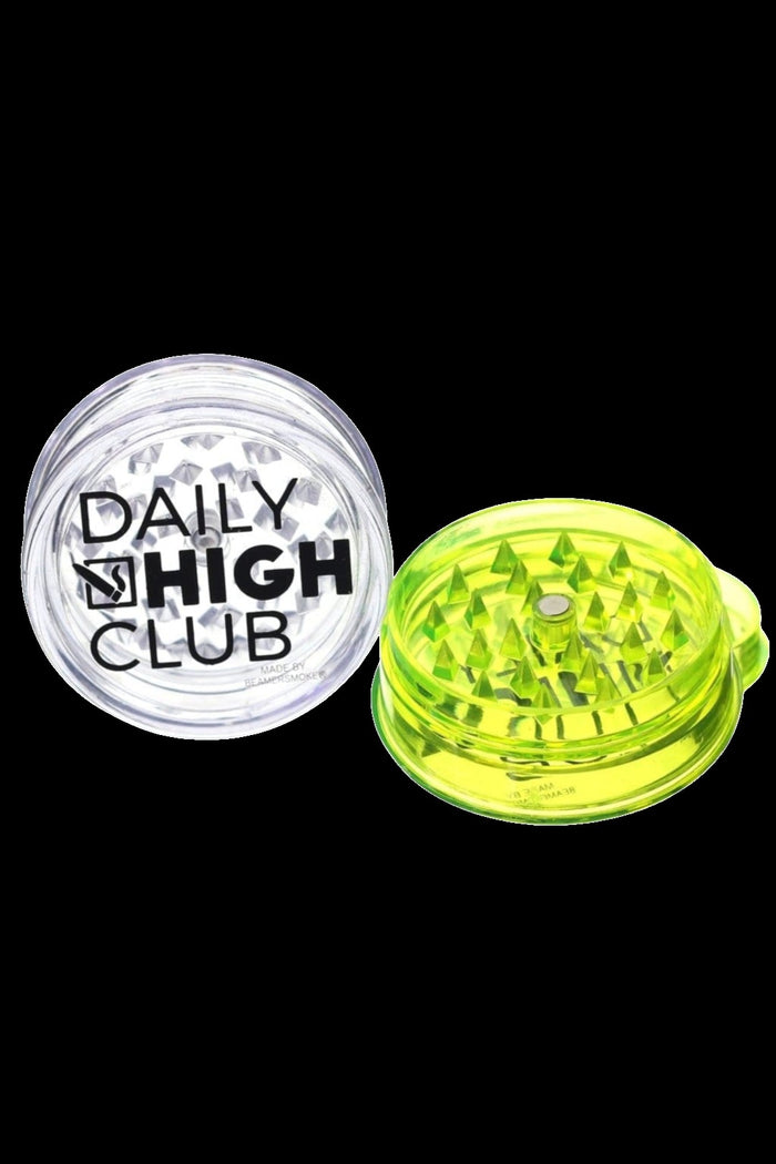 Two cannabis grinders, one clear with "Daily High Club" text and one neon green, isolated on a white background.