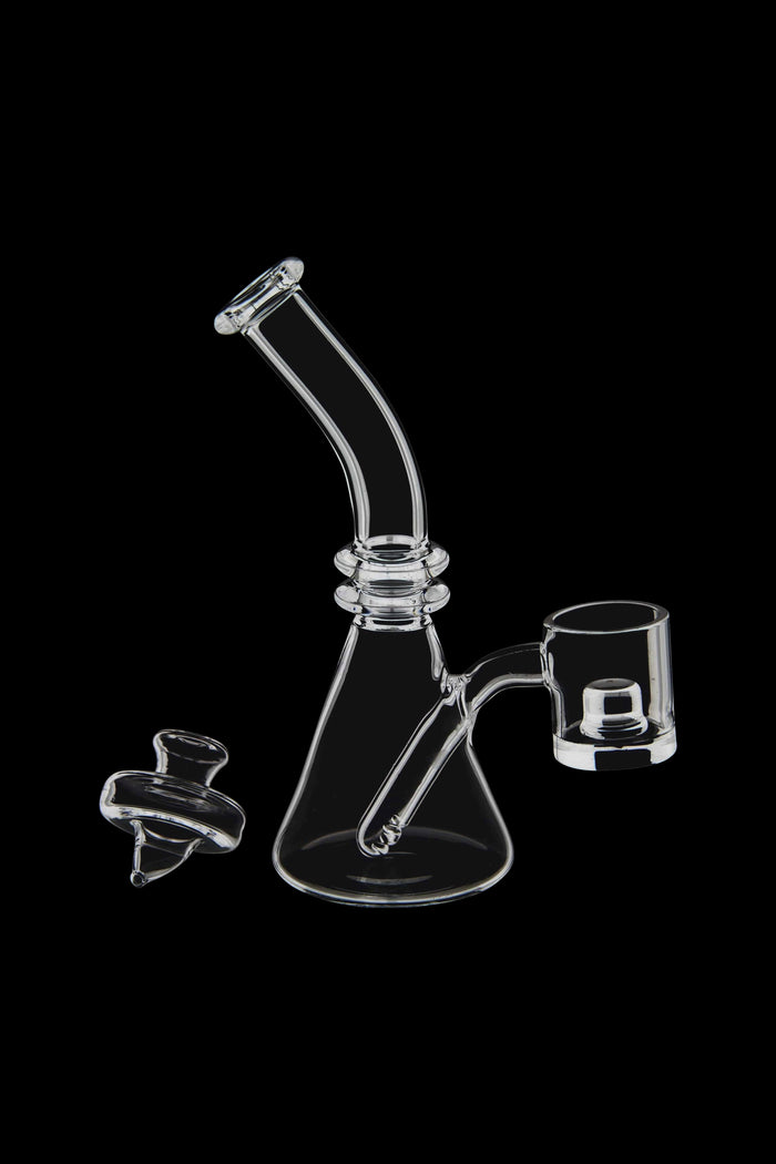 Clear glass dab rig with a quartz banger and carb cap, isolated on a black background.