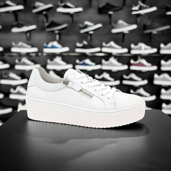 White leather platform sneakers with lace-up and side zipper, shown on a shoe display