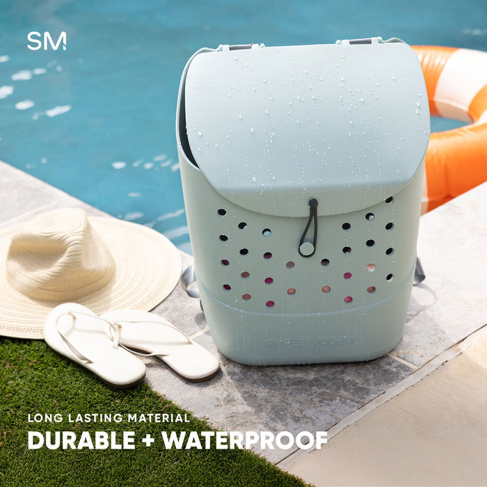 White PT02 Getaway Backpack with black and burgundy ventilation holes displayed poolside with water beads, surrounded by sun hat, sandals, and orange float. Text reads "Long Lasting Material - Durable + Waterproof."